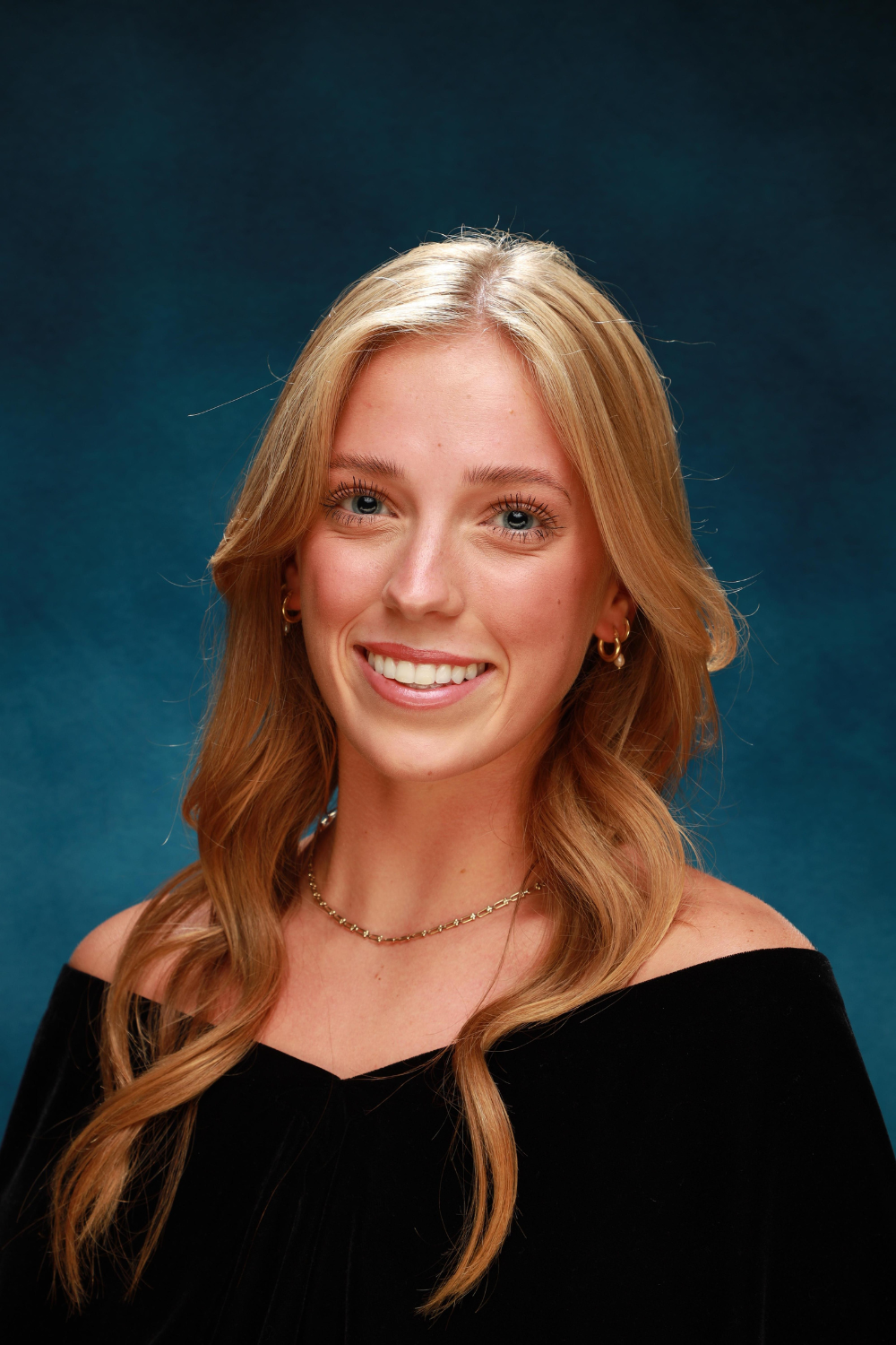 Teenage girl wearing an off the shoulder black shawl against a blue background.
