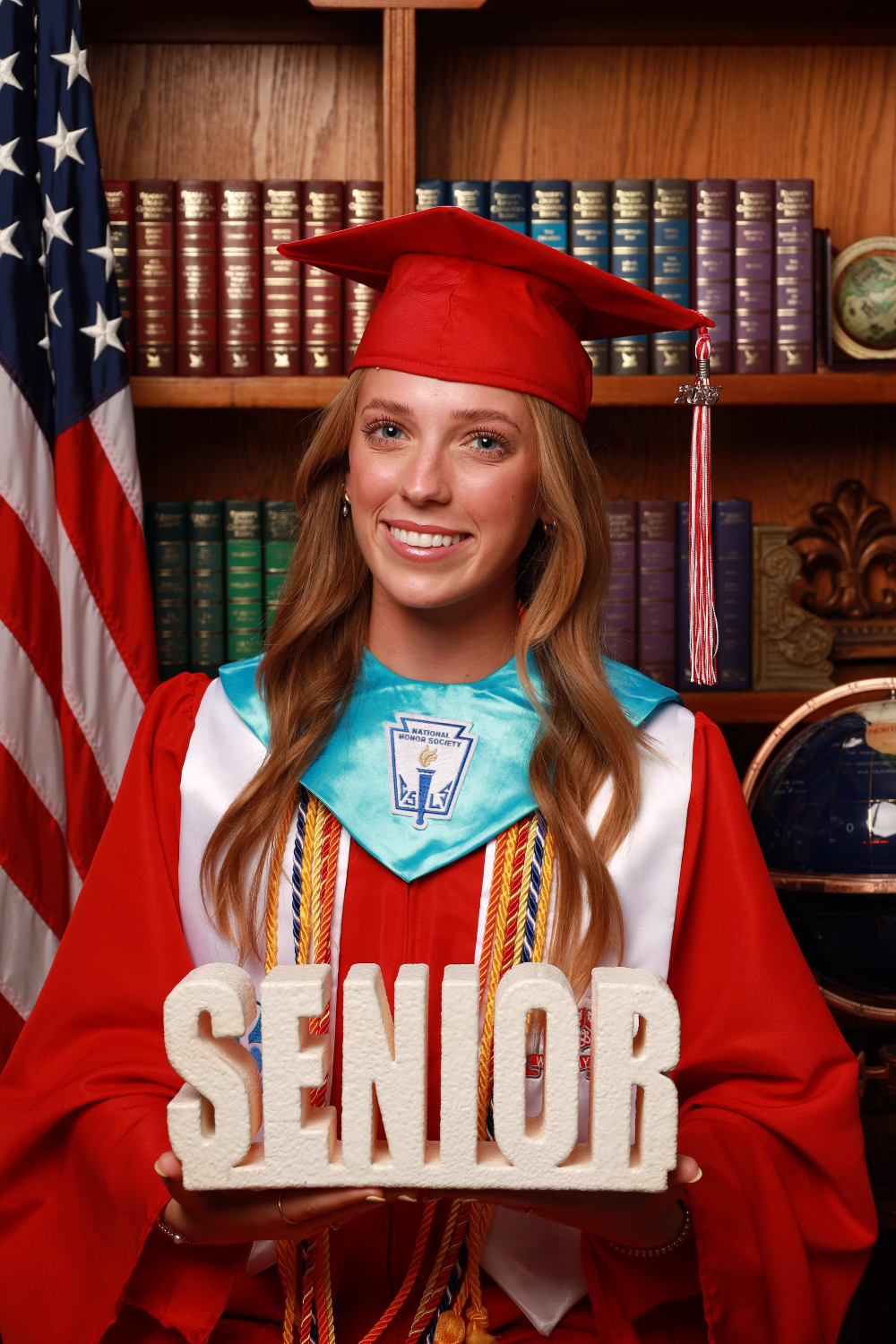 Female graduate wearing a red graduation cap and gown holding a sign reading "senior".