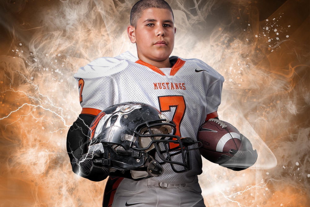 Youth football player posing with a helmet and football under each arm